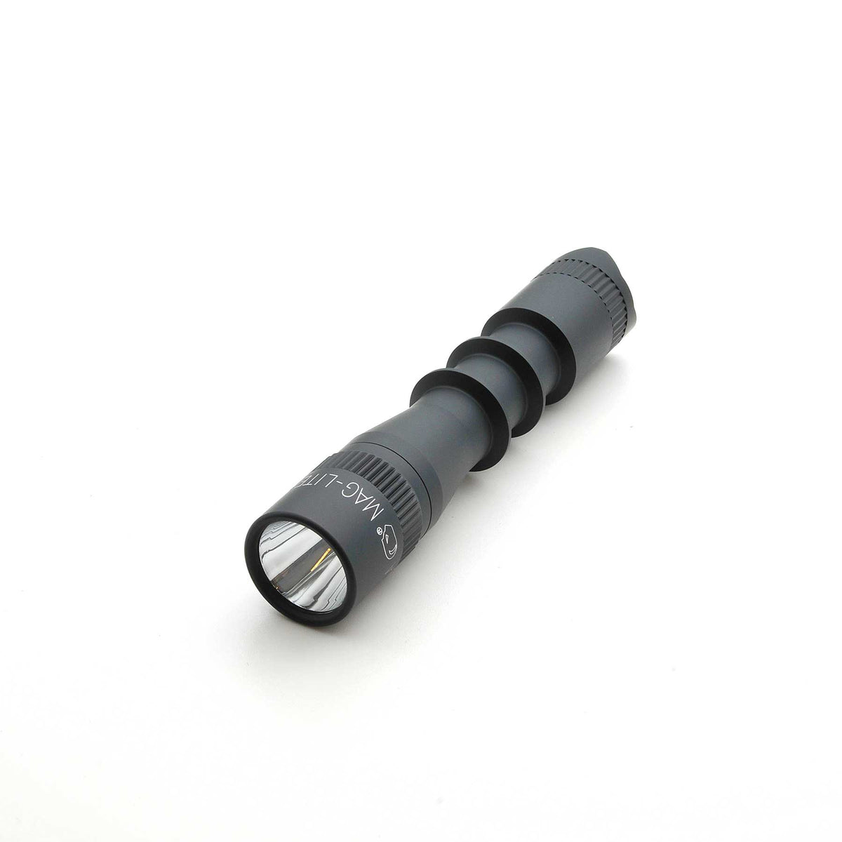 Angled view of MAG-TAC 2 TL Black Plain Bezel flashlight highlighting the ridged body and reflective lens.