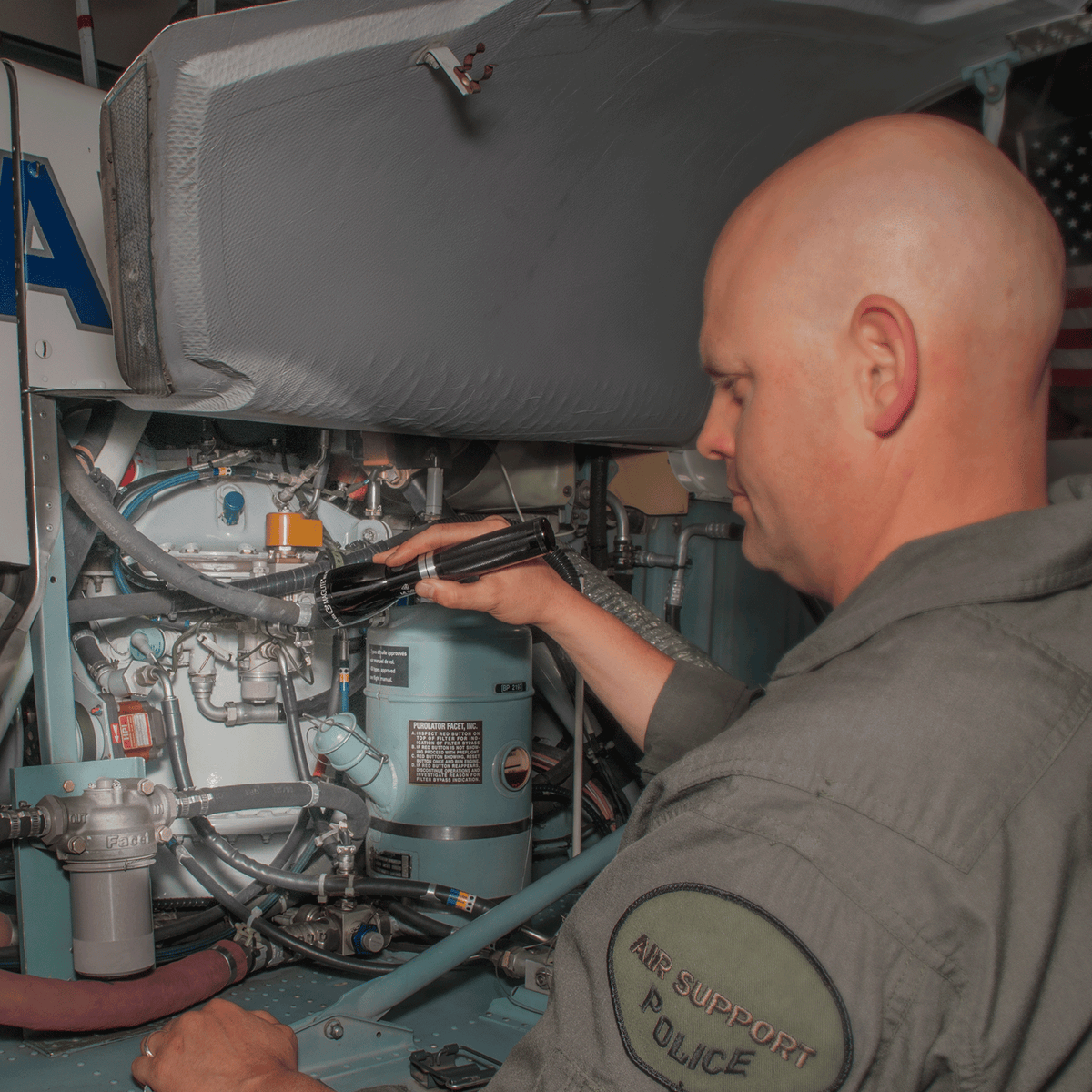 Technician in uniform using a Maglite flashlight to inspect machinery in a workshop