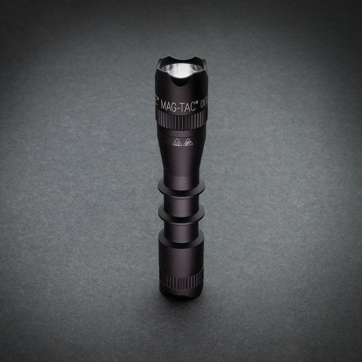 Top view of black MAG-TAC flashlight head with crown bezel against gray background