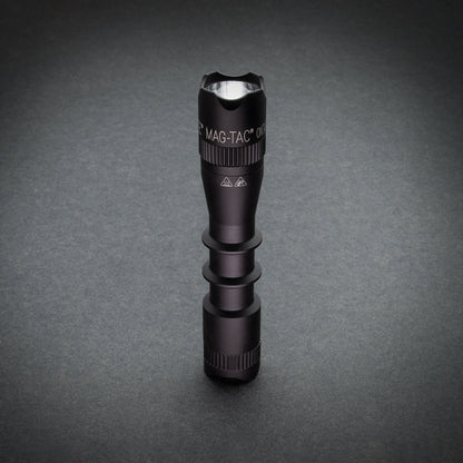 Top view of black MAG-TAC flashlight head with crown bezel against gray background