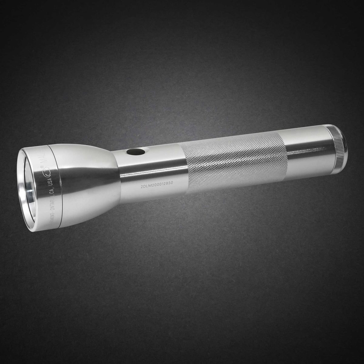 Gray ML300L LED 2-Cell D flashlight with knurled grip shown diagonally from the opposite side on a dark surface