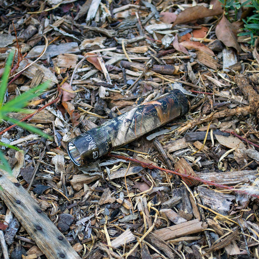 Maglite XL50 flashlight in Mossy Oak New Country DNA camouflage resting on wood chips